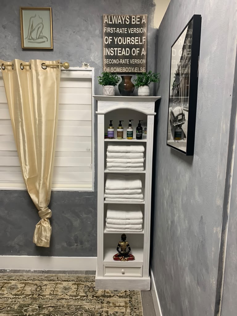 Fresh white towels and spa essentials neatly arranged on a white shelf beside a gold silk curtain